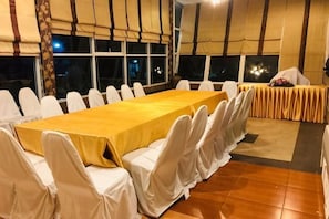 A conference room with a long table, white chairs, and a window with a view of the night sky. - Baansuan Greenview Resort And Spa (Khon Kaen)