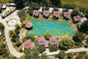 An aerial view of a resort with a central swimming pool surrounded by multiple buildings with red roofs.