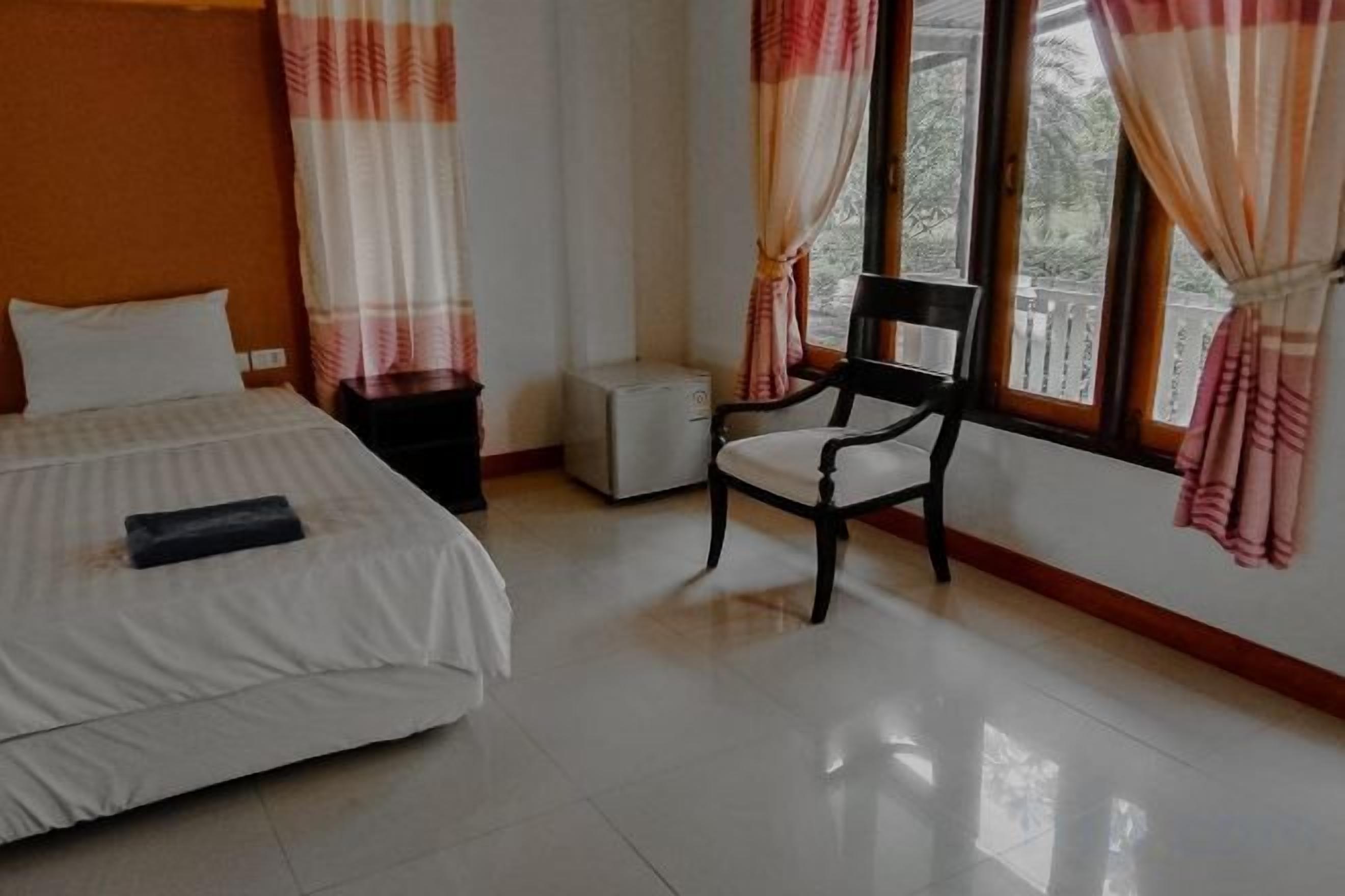 Una habitación de hotel con una cama, una silla, una mesita y una ventana con cortinas.