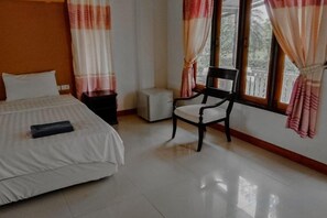 Una habitación de hotel con una cama, una silla, una mesita y una ventana con cortinas.