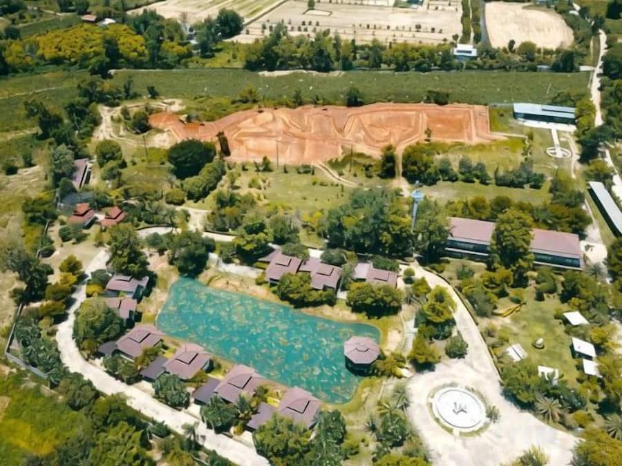 An aerial view of a resort with a swimming pool, multiple buildings, and surrounding greenery.