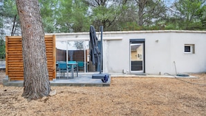 Een laag, gelijkvloers gebouw met een houten omheining, een terras met tuinmeubilair en een duidelijke deur.