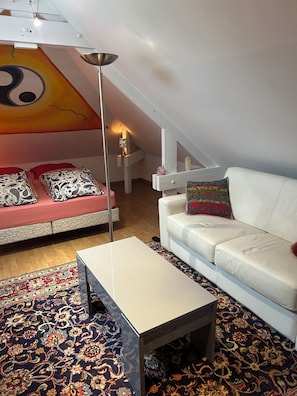 Ein modernes Loft-Apartment mit hohen Decken, einem großen Fenster, einem weißen Sofa, einem weißen Sessel, einem Couchtisch und einem farbenfrohen Teppich.