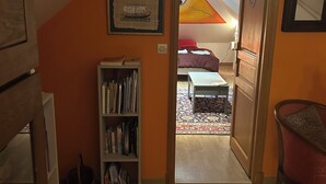 A room with a sloped ceiling, a bookshelf, a patterned rug, and a door leading to another room with a bed and a colorful wall hanging. - Large, comfortable room, parking spaces, pets welcome, bicycle garage (Étaples)