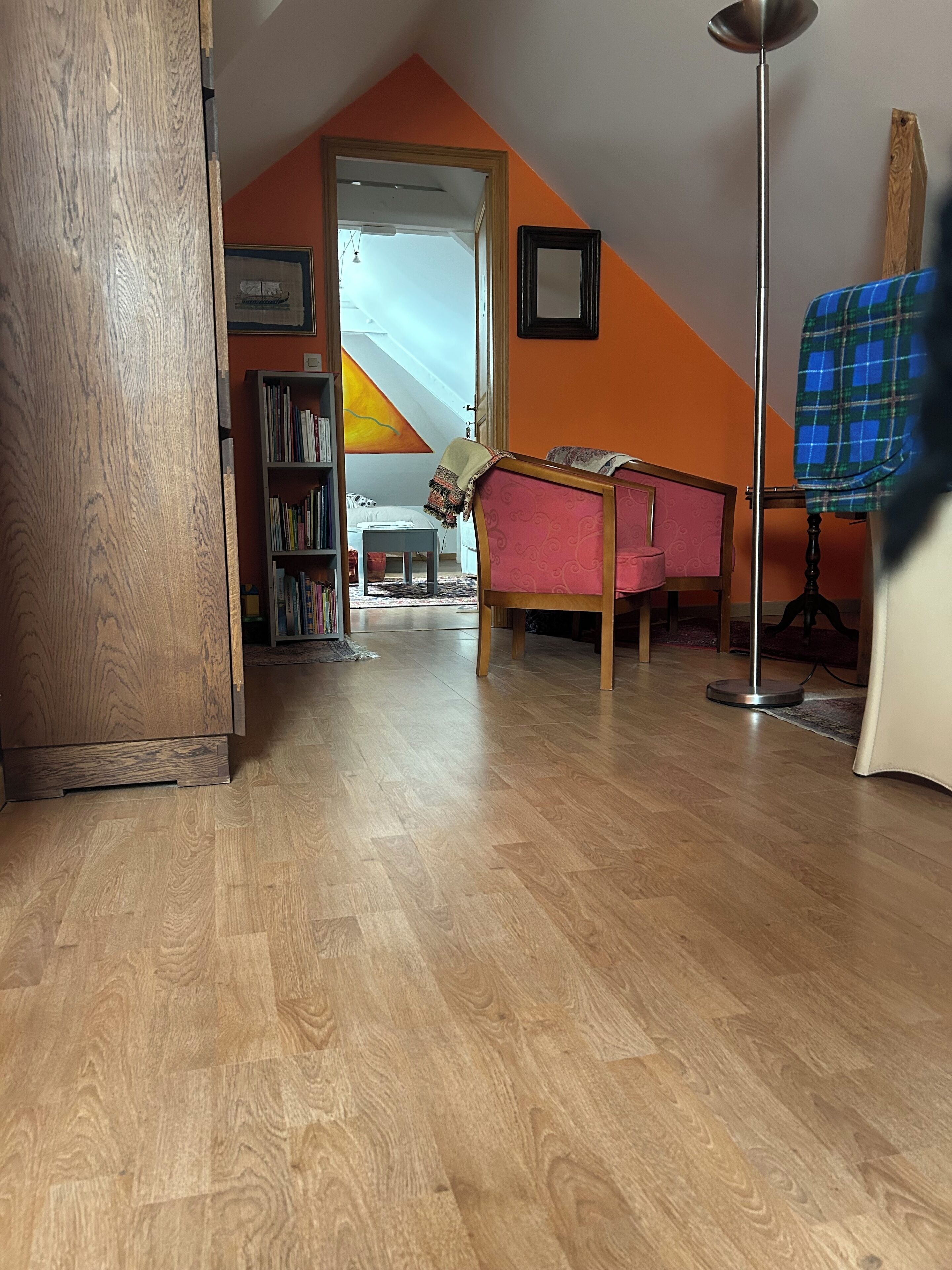 A room with a wooden floor, a pink sofa, a bookshelf, and a framed picture on the wall.