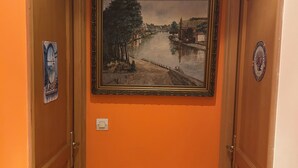 A hallway with two wooden doors, an orange wall, and a framed painting of a riverside scene. - Large, comfortable room, parking spaces, pets welcome, bicycle garage (Étaples)