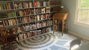 Ein Zimmer mit einer großen Bücherwand, einem Holztisch und einem gemusterten Teppich.