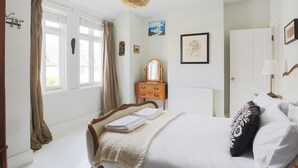 Ein Schlafzimmer mit Bett, Schminktisch, Spiegel, Heizkörper und einem Fenster mit Vorhängen.