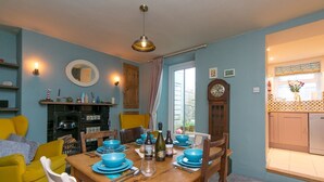 A dining area with a wooden table set for four, surrounded by yellow chairs. A fireplace with a tiled surround is visible in the background. - Cottage close To Coastal Path & Puffin Island | Pass the Keys (Beaumaris)