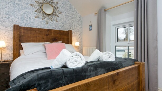 A bedroom with a wooden headboard, a bed with white and pink pillows, a star-shaped mirror, and a window with curtains. - Cottage close To Coastal Path & Puffin Island | Pass the Keys (Beaumaris)