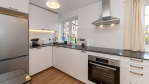A modern kitchen with white cabinets, a stainless steel range hood, a built-in oven, and a window with a view of the outside.