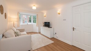 A modern living room with a white sofa, a flat-screen TV on a white cabinet, a large window with curtains, and a white door.
