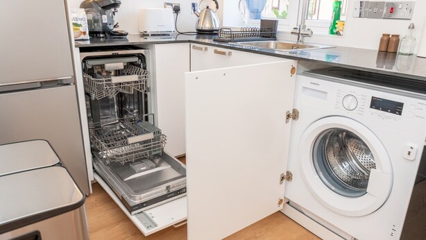 A compact kitchen with a dishwasher, a washing machine, and a kettle.