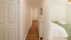A narrow hallway with a wooden floor leading to a bedroom.