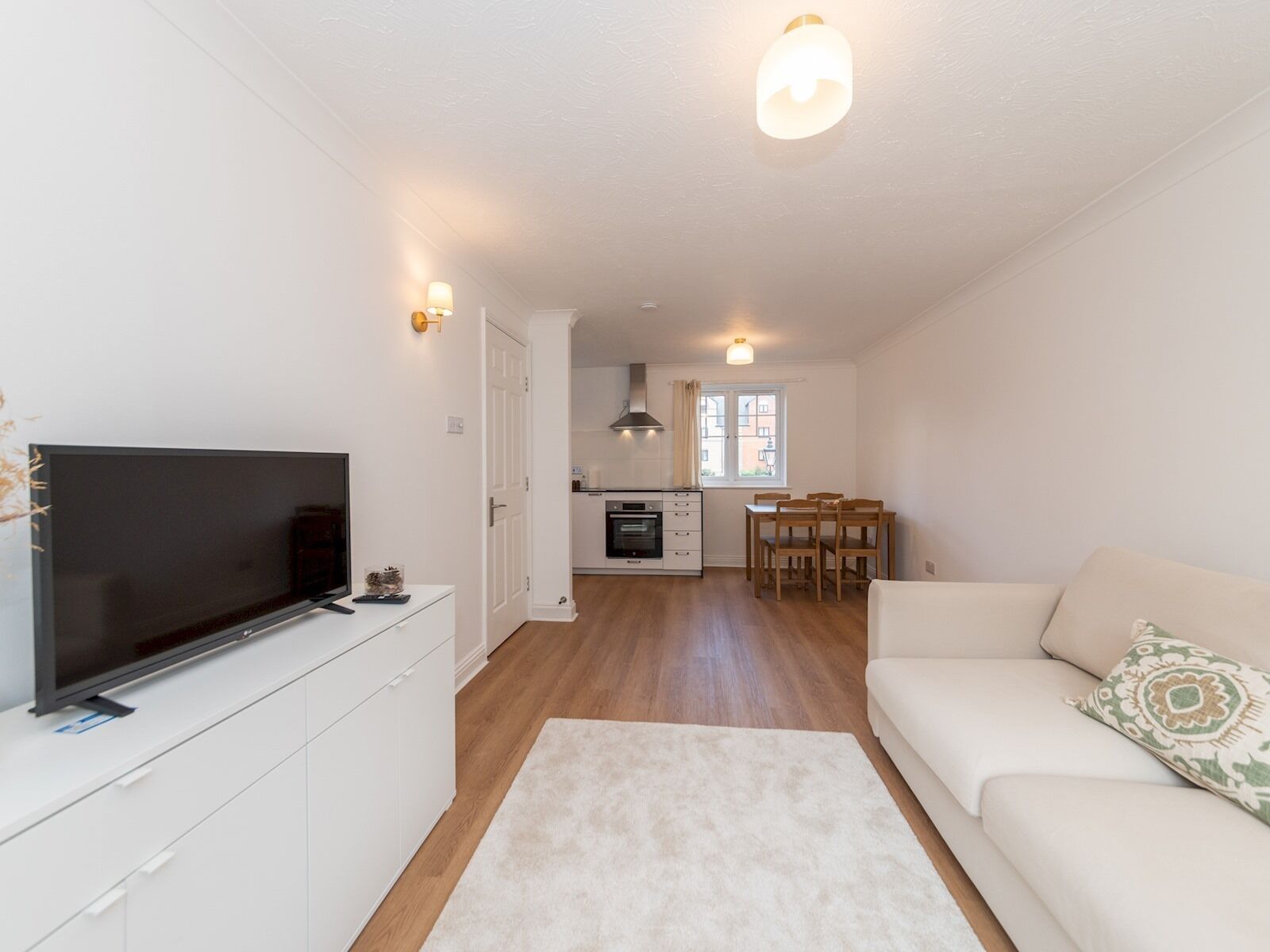 Uma sala de estar moderna com televisão de tela plana, um sofá branco e um espaço de refeições com mesa e cadeiras.