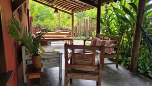 Un patio exterior con mobiliario de madera, incluyendo un banco y una mesa, rodeado de abundante vegetación.