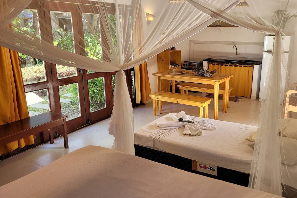 Quarto com cama de dossel, mesa de madeira e um banco.
