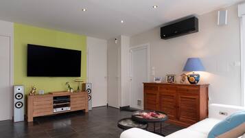 Ein Wohnzimmer mit Flachbildfernseher, einem Holzkasten, einer Couch und einer Lampe.