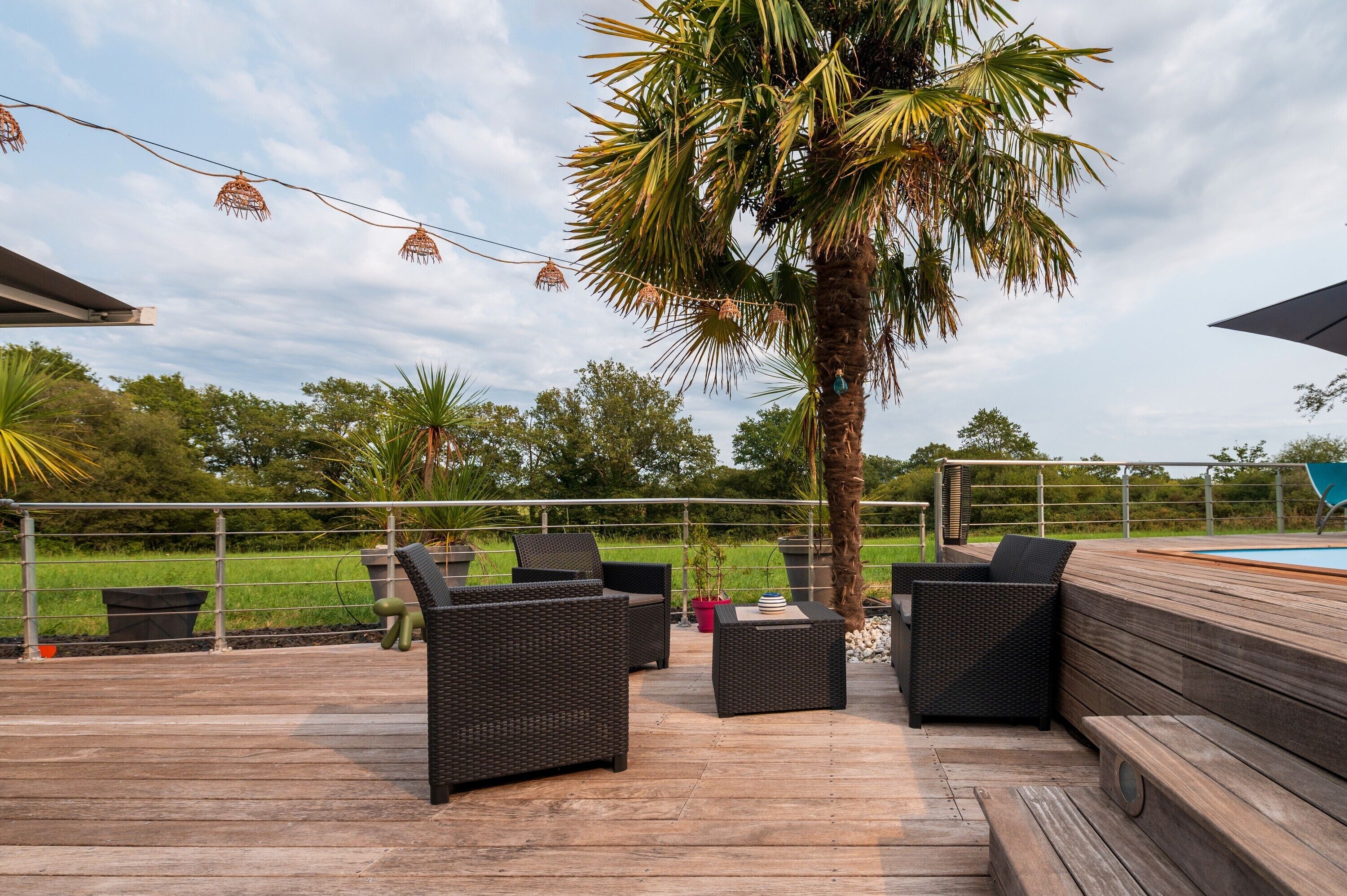 Une terrasse extérieure avec des meubles en osier, un palmier et une piscine en arrière-plan.