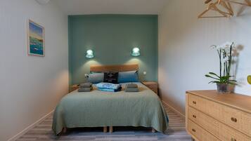 Une chambre à coucher comprenant un lit, des tables de chevet, une commode, un climatiseur fixé au mur, un tableau encadré et un luminaire suspendu.