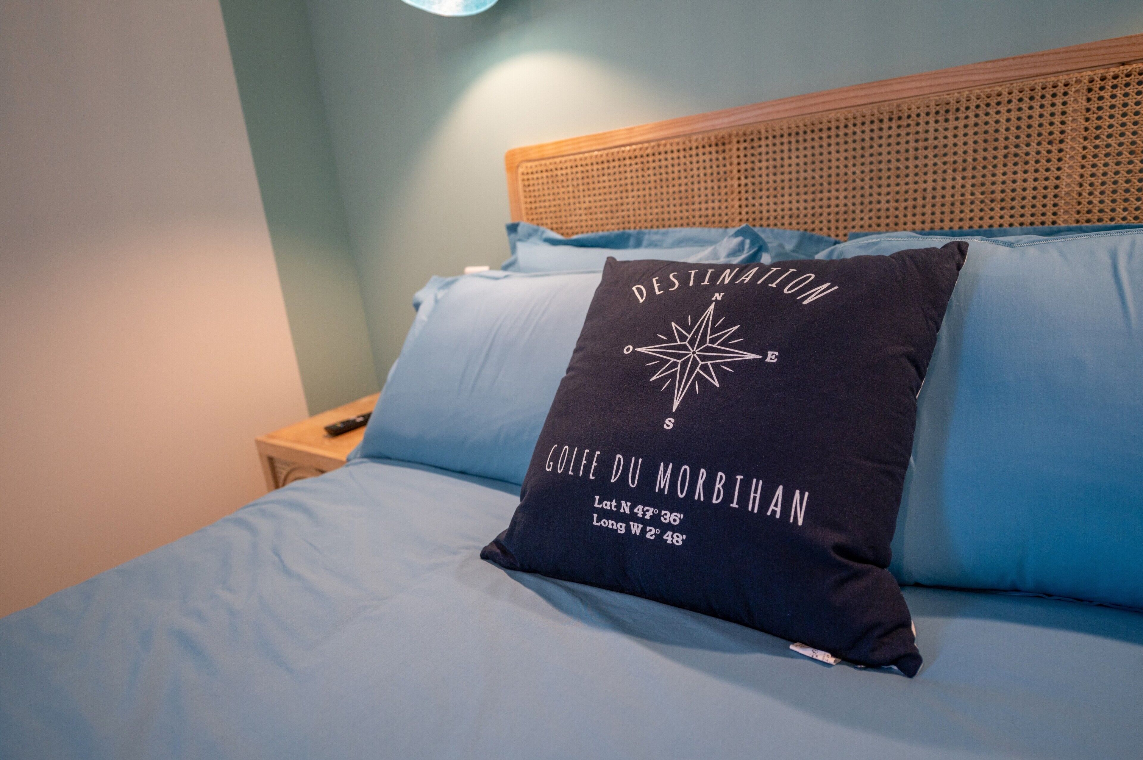 Un lit avec une couvre-lit bleue, un oreiller orné d’un motif de boussole et une tête de lit en bois.