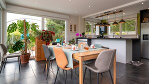 A modern kitchen with a dining area, large windows, and potted plants.