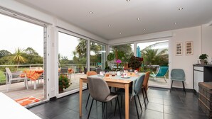 A spacious dining area with a table set for four, a sliding glass door leading to a balcony, and a kitchen area visible to the right.
