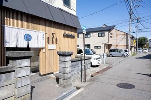 Vista de una calle con un edificio de fachada de madera y un letrero que indica un restaurante. Hay coches estacionados a lo largo de la calle y un cielo despejado.