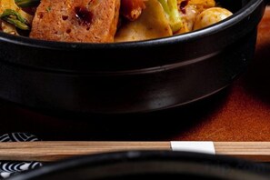 Ein Detailfoto eines Gerichts in einer schwarzen Schüssel, möglicherweise ein Eintopf oder Curry, mit sichtbaren Gemüsesorten und einem Stück Brot.