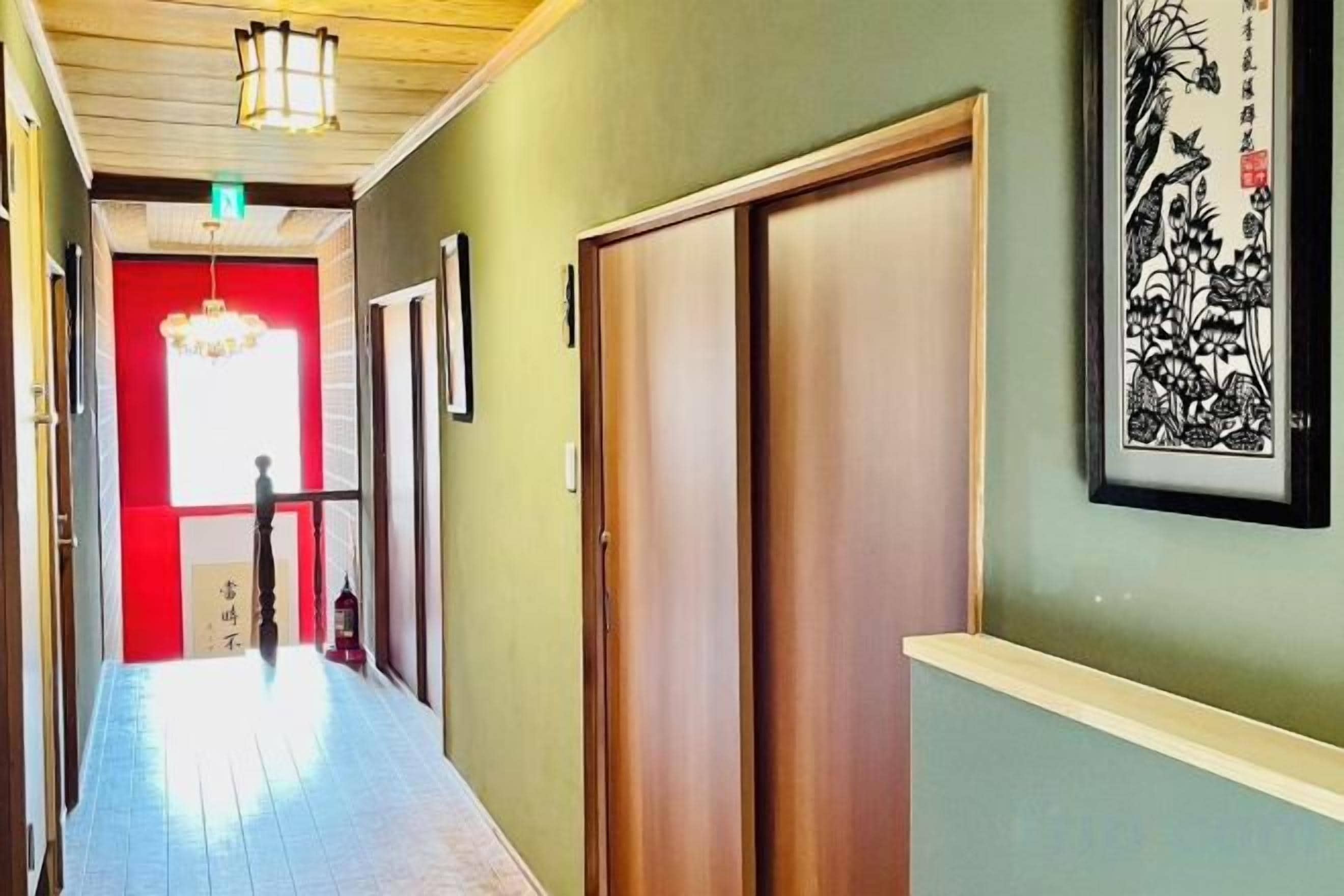 A hallway with a wooden door, a framed artwork, and a red door in the background.