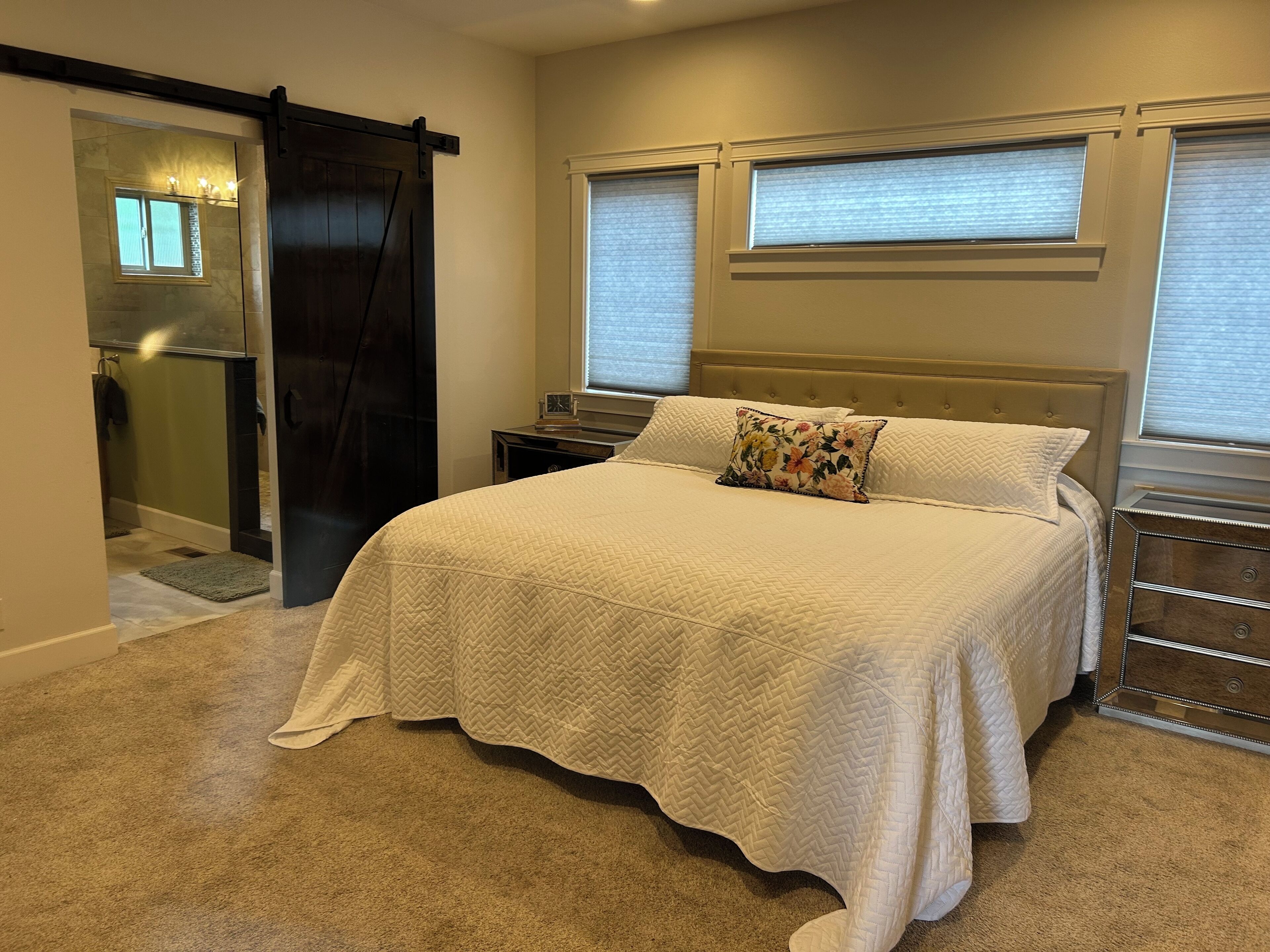 A bedroom with a large bed, a nightstand, a dresser, a sliding door, and a window with blinds.