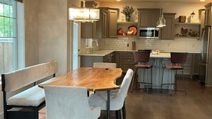 Une cuisine moderne avec une table à manger en bois, des tabourets de bar et une grande fenêtre.