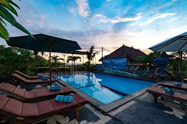 A swimming pool with lounge chairs and umbrellas, surrounded by tropical plants and a sunset view. - Sedok Jineng Villa Lembongan (Lembongan Island)