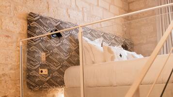A loft bedroom with exposed brick walls, a wooden ceiling, and a glass railing.