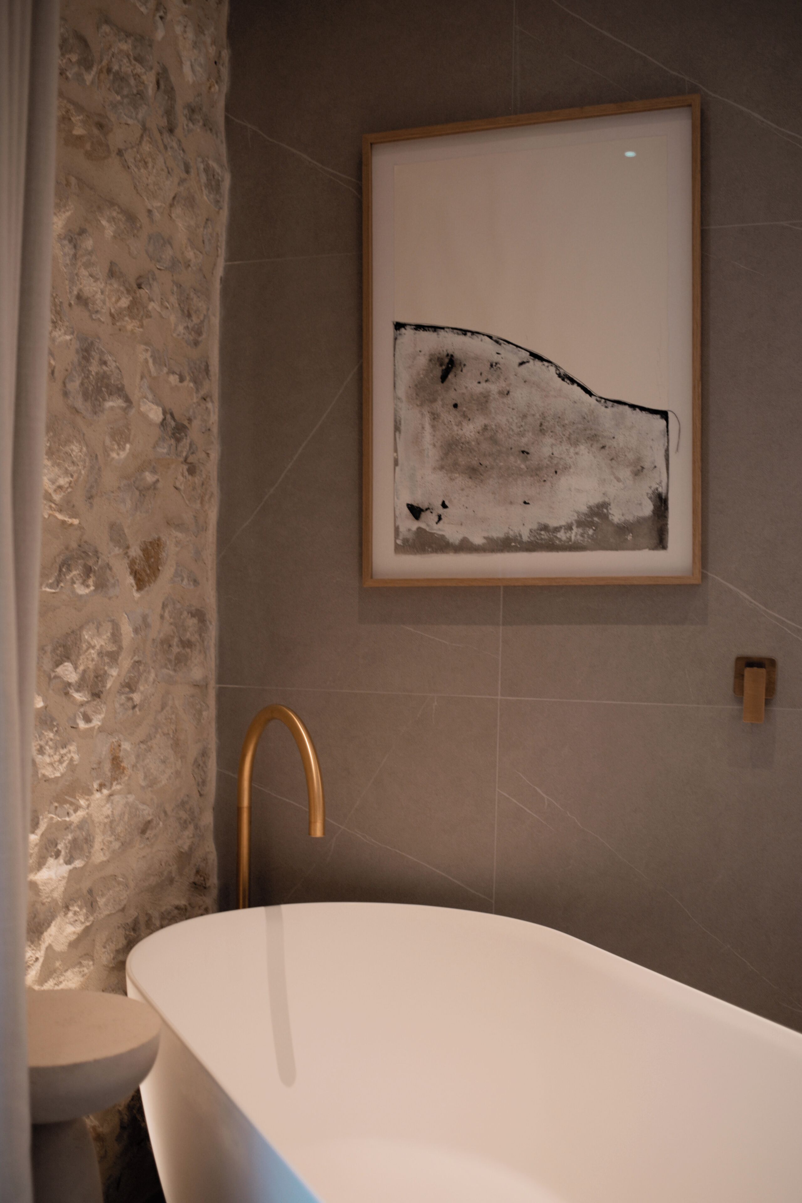 A modern bathroom with a freestanding bathtub, a stone wall, and a framed abstract painting on the wall.