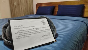 A bed with a blue bedspread and a framed note on it. - Makorn Nonkleng (Thung Song)