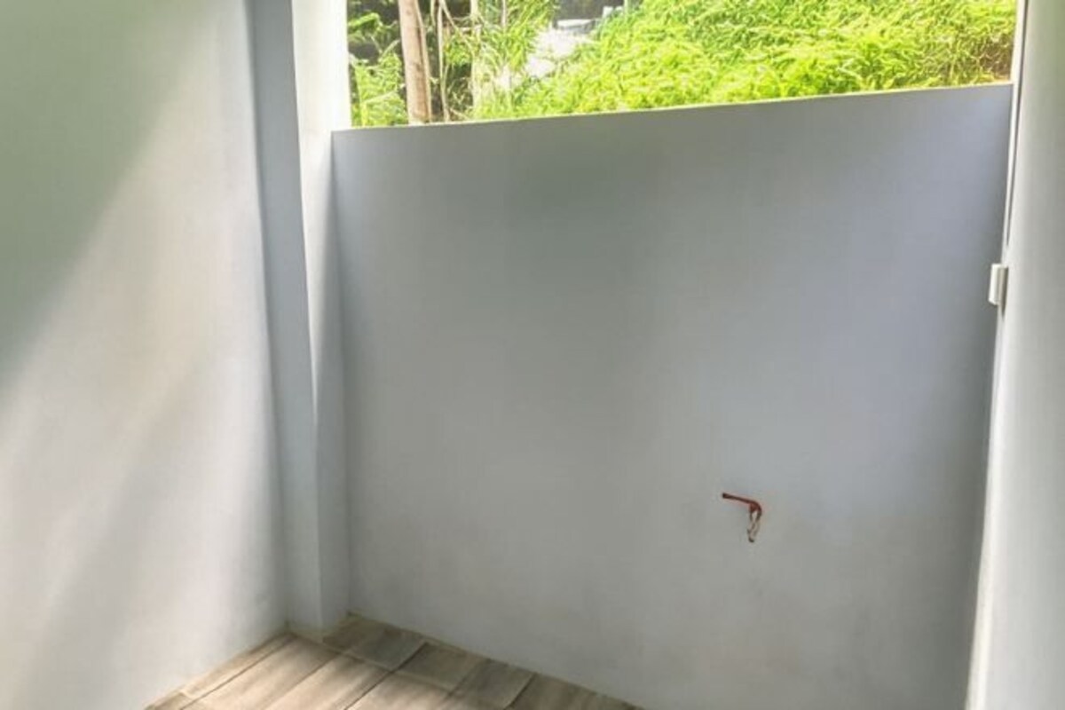 A room with a wooden floor, a white wall, and a small red object on the wall.