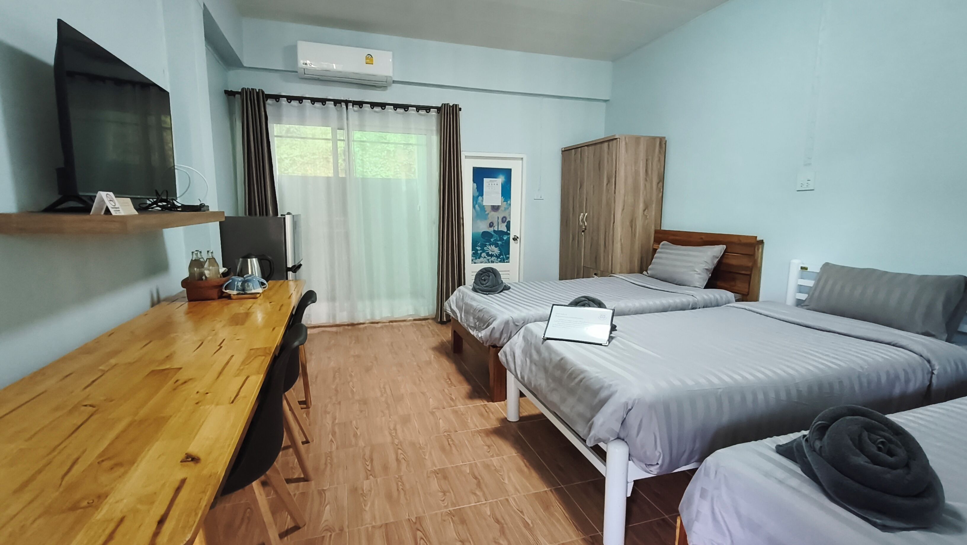 A hotel room with two beds, a wooden desk, a television, and an air conditioning unit.