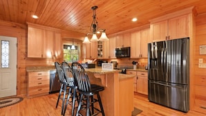 A wooden-paneled kitchen with a stainless steel refrigerator, granite countertops, and a central island with bar stools.