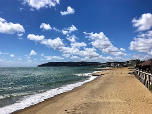 Ein Strand mit einer Holzpromenade, einem Steg und Gebäuden im Hintergrund.