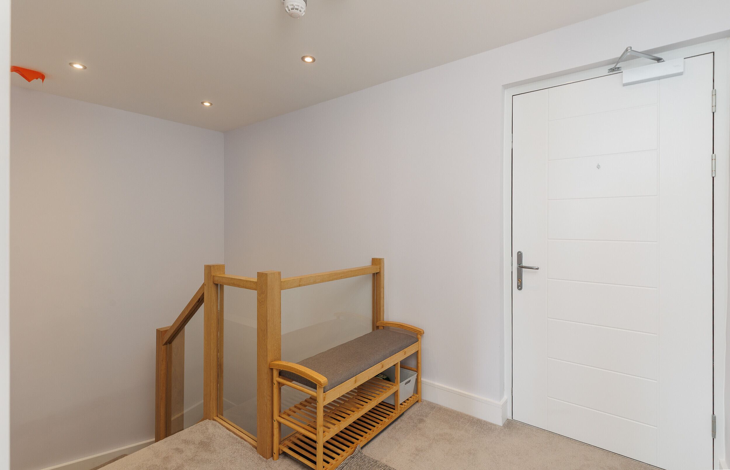 Een kamer met een houten bank, een witte deur en een plafondlamp.