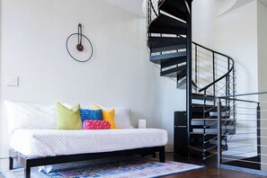 A bedroom with a bed, colorful pillows, a patterned rug, a black spiral staircase, and a wall-mounted light fixture. - *NEW Central Austin | Sleeps 12 - WalkerVR Firefly (Austin)