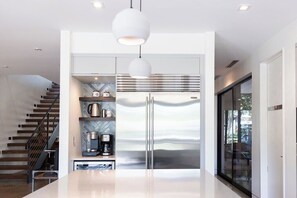 A modern kitchen with a stainless steel refrigerator, pendant lighting, and a herringbone-patterned backsplash.