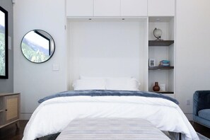 A bedroom with a bed, a round mirror, a shelf with a globe, and a view of greenery. - *NEW Central Austin | Sleeps 12 - WalkerVR Firefly (Austin)