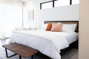 A neatly made bed with white and brown bedding, a wooden bench, and a framed picture on the wall. - *NEW Central Austin | Sleeps 12 - WalkerVR Firefly (Austin)