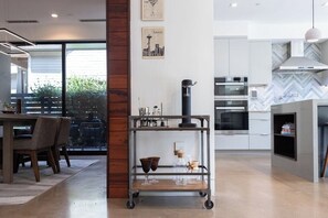 A modern kitchen with stainless steel appliances, a coffee machine, and a dining area with a wooden table and chairs. - *NEW Central Austin | Sleeps 12 - WalkerVR Firefly (Austin)