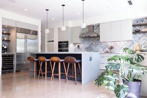 A modern kitchen with a central island, bar stools, stainless steel appliances, and a herringbone-patterned backsplash.