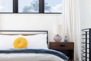 A bedroom with a bed, a bedside table with a lamp, and a window with curtains.