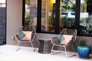 Two wicker chairs with cushions, a small round table, and a potted plant outside a building with large windows.