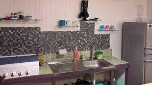 A kitchen with a gas stove, sink, and a refrigerator. There are various kitchen items on the counter and shelves. - Air conditioned home w/ full kitchen, TV & parking (Puerto Viejo de Talamanca)
